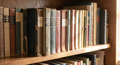 A wooden shelf of old postcard albums in a home library with worn spines and soft afternoon light
