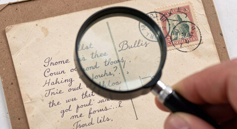 Close view of a magnifying glass held over an old postcard showing a handwritten message and a postmark.